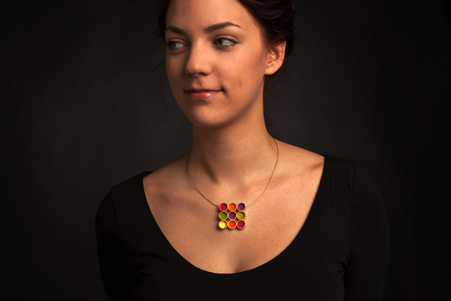 Modell mit auffälligem Gold-Plattiertem Halsschmuck, 9 Kreise im Quadrat gefüllt mit farbigem Filz, alles vor schwarzem Hintergrund